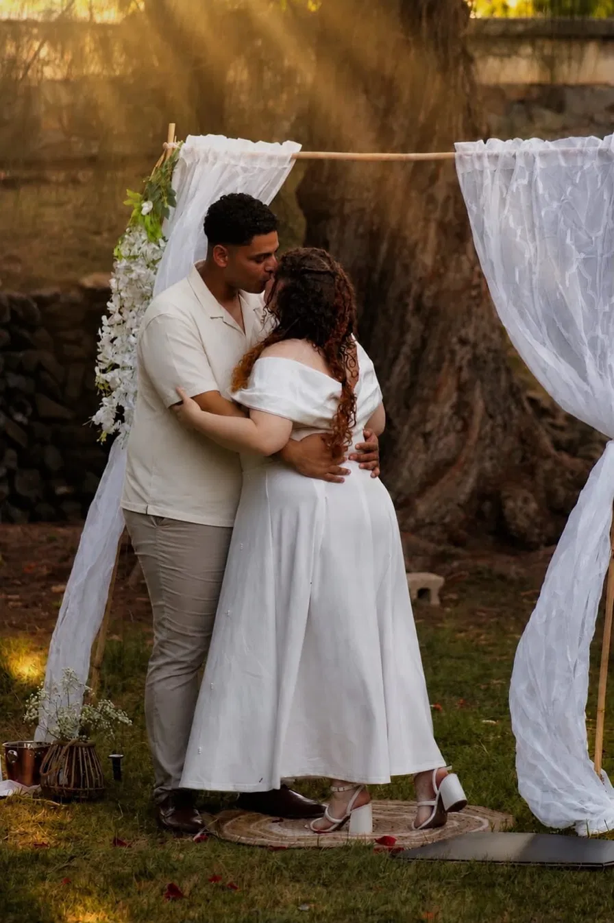 Michael y Arianne abrazados bajo un árbol grande, con rayos de sol entrando entre las ramas